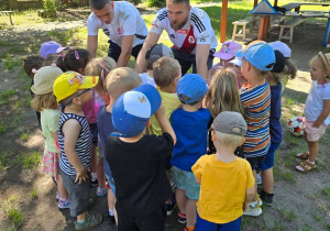 Dzieci stoją w grupie tyłem i przybijają piątkę piłkarzom.