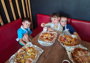 Dzieci siedzą przy stołach w pizzerii i próbują pizz wykonanych przez siebie.