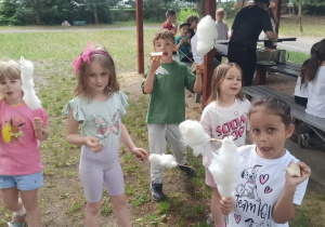 Dzieci pożyją do zdjęcia w ogrodzie przedszkolnym, w rękach trzymają watę cukrową.