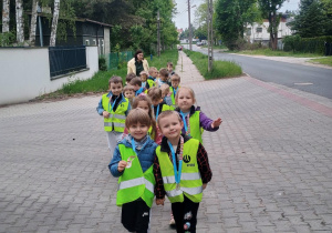 Uśmiechnięte dzieci idą parami w kamizelkach odblaskowych.