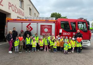 Zdjęcie grupowe dzieci z całego przedszkola wraz z kadrą i strażakami na tle wozy strażackiego.
