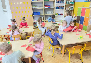 Dzieci siedzą przy stołąch wycinają serca z papieru