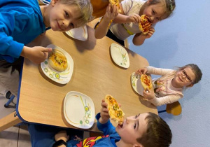Piątka dzieci siedzi przy stolikukażde zjada pizze którą wcześniej wykonało