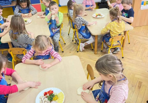 Grupa dzieci siedzi przy stolikach każde dziecko robi swoją pizze
