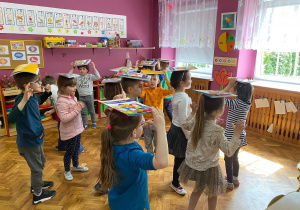 Dzieci ćwiczą równowagę chodząc z książka na głowie.