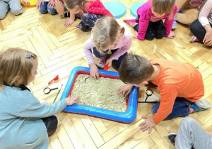 Dzieci bawią się w archeologa, szukają kości dinozaura w ziemi.