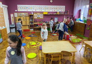 Zabawa w szukanie figur geometrycznych. Dzieci podzielone na grupy odnajdują w klasie przedmioty o danym kształcie.