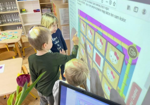 Dzieci przy tablicy multimedialnej grają w grę memory. Ćwiczą spostrzegawczość i pamięć a także współpracę