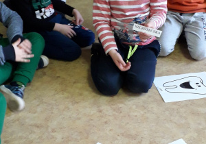 Zajęcia w grupie starszaków. Dzieci siedzą w kole, na podłodze porpzkładane obrazki i napisy związane ze stomatologiem. Chłopiec odczytuje wybrany wyraz.
