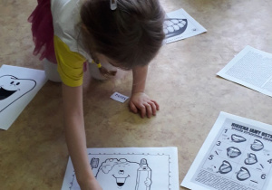 Zajęcia w grupie starszaków. Dzieci siedzą w kole, na podłodze porozkładane obrazki i napisy związane ze stomatologiem. Jedno z dzieci dopasowuje podpis do obrazka.