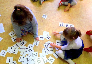 Dziewczynki siedzą na podłodze wśrod liter, szukają tych z których mogą ułożyć napis "dentysta"
