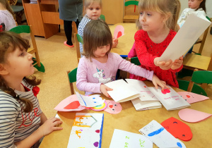 Dziewczynki z grupy średniej siedzą przy stoliku w sali i oglądają otrzymane kartki walentynkowe