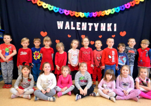 Zdjęcie grupowe. Dzieci ze średniej grupy pozują w sali na tle dekoracji z napisem WALENTYNKI. Ubrane są na czerwono.
