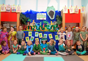 Zdjęcie grupowe. Dzieci z najmłodszej grupy pozują na tle dekoracji z okazji Dnia dinozaura.