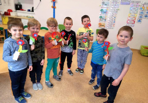 Chłopcy z grupy 4,5 - latków stoją w półkolu, trzymają w rękach wlasnoręcznie zrobione kwiaty.