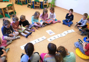 Dzieci siedzą na podłodze, wokół ułożonego z liter napisu DZIEŃ KSIĄŻKI.