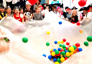 Zabawa "sztorm" - dzieci podrzucają piłeczki rozrzucone na wielkiej płachcie folii.