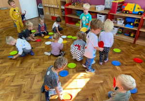 Dzieci z grupy maluszków układają kropki z papierowych talerzyków na podłodze w sali.