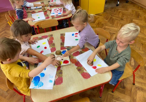 Dzieci stemplują kropki odciskając ziemniaki w kolorowej farbie.