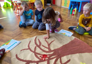 Dziewczynka odciska swoją dłoń umoczoną w farbie na papierze z narysowanym drzewem