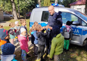 Grupa dzieci stoi przy Policjancie i radiowozie.