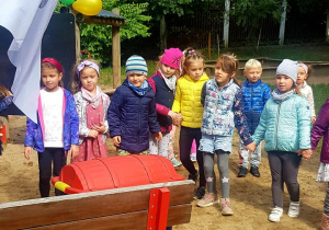 Dzieci zebrane w kole w ogrodzie przedszkolnym. Pośrdoku na ławce stoi odnaleziona wcześniej skrzynia ze skarbem.