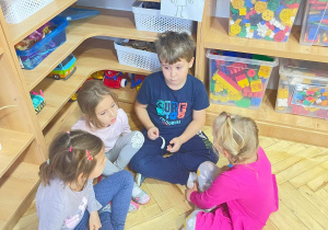 Czworo dzieci siedzi na podłodze, pracują w grupach. Nad nimi rysunek wyrażający emocje.