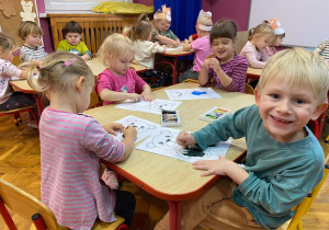 Dzieci siedzą przy stolikach. Kolorują obrazki z misiem.