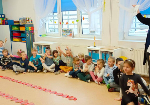 Dzieci siedzą w kole na podłodze. Nauczycielka wyczutuje ile kasztanów zebrała każda z grup.