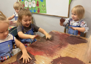 Dzieci mieszają farby dłońmi na blacie biurka.