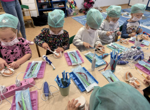 Dzieci w czepkach i maskach, bawią się w stomatologów.