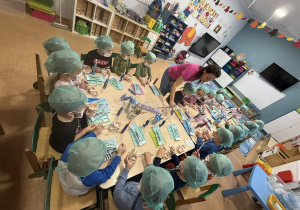 Dzieci w czepkach i maskach bawią się narzędziami stomatologicznymi.