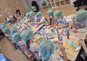 Dzieci w czepkach i maskach bawią się narzędziami stomatologicznymi.