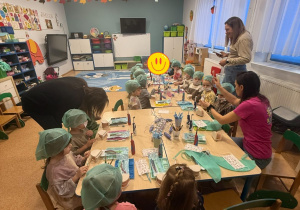 Dzieci w czepkach i maskach bawią się narzędziami stomatologicznymi.