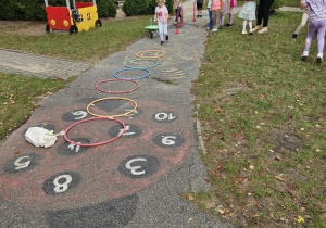 Dzieci skaczą przez przeszkody w ogrodzie przedszkolnym.