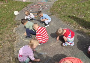 Dzieci ryują kredą po betonie w ogrodzie przedszkolnym.