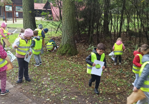 Dzieci w odblaskowych kamizelkach szukają darów jesini.