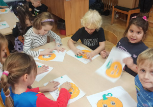 Dzieci tworzą pracę plastyczną, wyklejają papierem dynie przy stolikach.