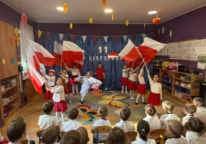 Zdjęcie przedstawia fragment przedstawienia z okazji Dnia Niepodległości. Dzieci tańczą z flagami.