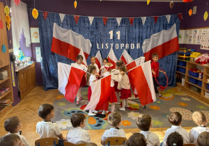 Zdjęcie przedstawia fragment przedstawienia z okazji Dnia Niepodległości. Dzieci tańczą z flagami.