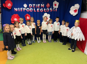 Dzieci stoją w półkolu na tle dekoracji z okazji Święta Niepodległości.