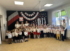Zdjęcie grupowe wszystkich dzieci i nauczycieli na tle dekoracji z okazji Święta Niepodległości.