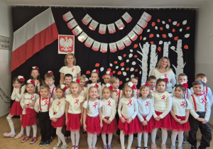 Zdjęcie grupowe dzieci i nauczycieli na tle dekoracji z okazji Święta Niepodległości.