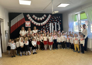 Zdjęcie grupowe wszystkich dzieci i nauczycieli na tle dekoracji z okazji Święta Niepodległości.