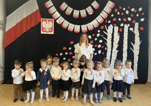Zdjęcie grupowe dzieci i nauczyciela na tle dekoracji z okazji Święta Niepodległości.