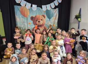 Grupa dzieci ustawione na tle ilustracji z misiem