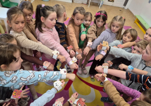 Dzieci wysuwają rączkę do przodu stojąc w kole, pokazują opaski na rękę z misiem