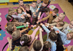 Dzieci wysuwają rączkę do przodu stojąc w kole, pokazują opaski na rękę z misiem