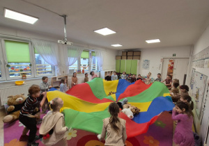 Dzieci stoją w kole i trzymają kolorową chustę animacyjną