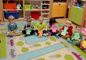 dzieci siedzą w kole na kolorowym dywanie i pokazują swoje prace plastyczne - wycięte misie.